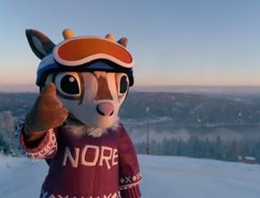 Maskot Nore Rein i skibakken, blå himmel, snø og utsikt over bygda - Klikk for stort bilde