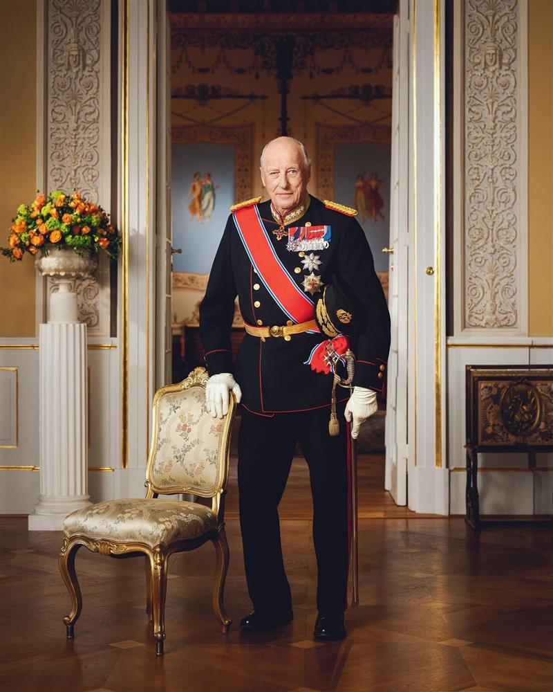 Kong Harald V står lent mot en stol med uniform - Klikk for stort bilde